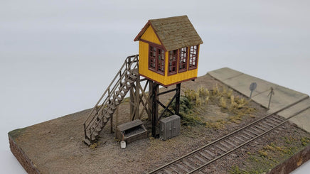 Model of a small wooden tower with a yellow roof on a miniature railway track setup.