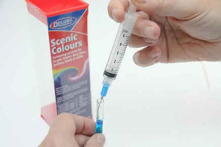 Person using a syringe to draw from a Scenic Colours packaging on a white background