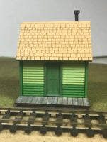 Model train station building with a green base and yellow roof on a track