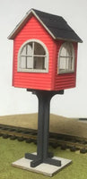 Red model train station on a stand with tracks in the background