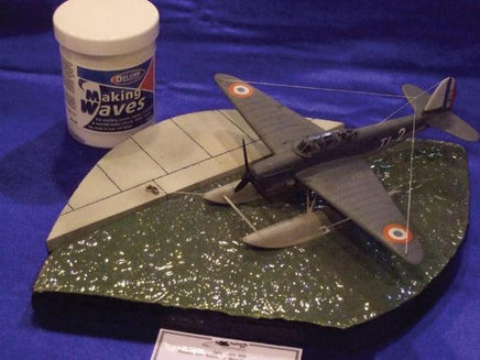 Model airplane on a blue surface with a container labeled 'Making Waves'.