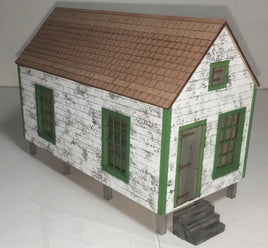 Model of a small house with a brown roof and green windows on a white background