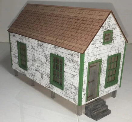 Model of a small house with a brown roof and green windows on a white background