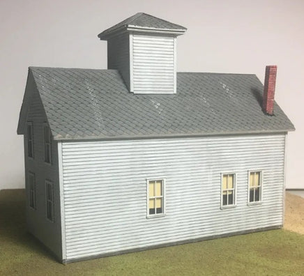 Model of a two-story building with a gray roof and white walls on a neutral background