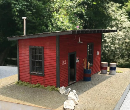 Model of a red building with a small garden in front, surrounded by greenery.