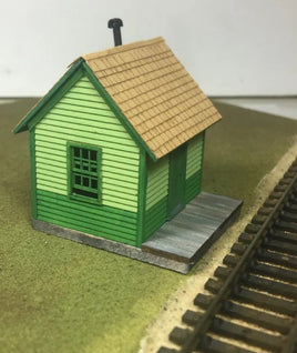 Model train station building next to railway tracks on a grassy surface.
