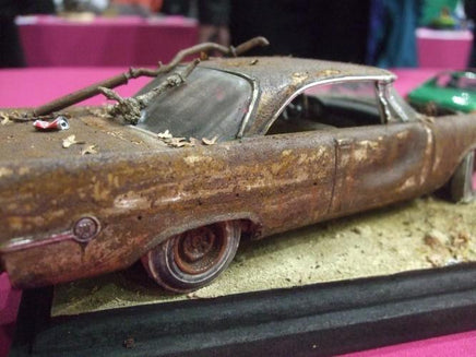 Rust-covered model car on a display stand with a pink background