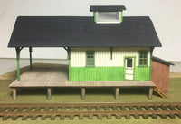 Model train station with green and white structure on a plain background