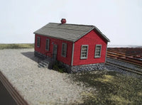 Model of a red building with a gray roof on a scale model railway track