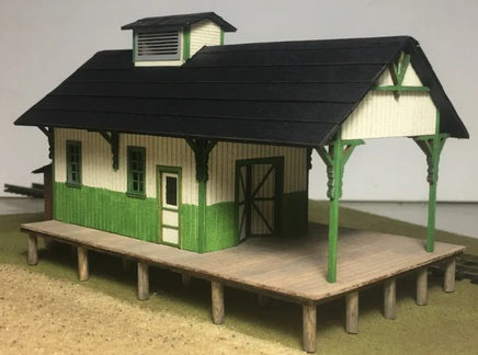Model of a small building with green and beige exterior on a plain background