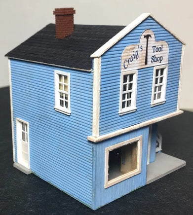 Model of a two-story building with a blue facade and 'Craig's Tool Shop' sign on a gray background