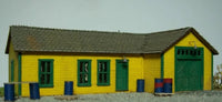 Small model building with a yellow exterior and green doors on a plain background