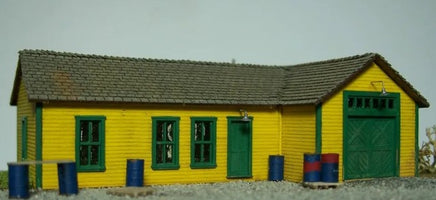 Small model building with a yellow exterior and green doors on a plain background