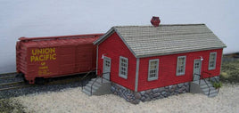 Model train set with a red building and Union Pacific boxcar on a track.