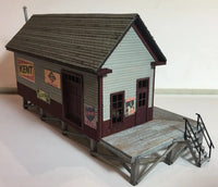 Model of a small building with a gray roof and wooden platform on a white background