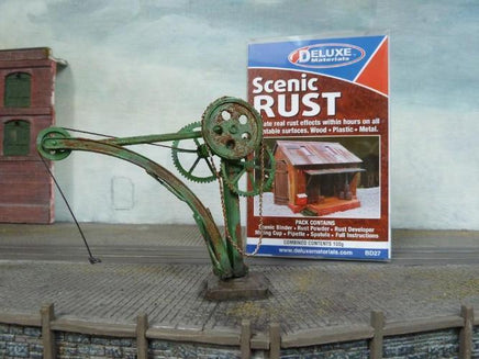 Model of a rusty mechanical arm on a miniature landscape with 'Deluxe Scenic Rust' product packaging.