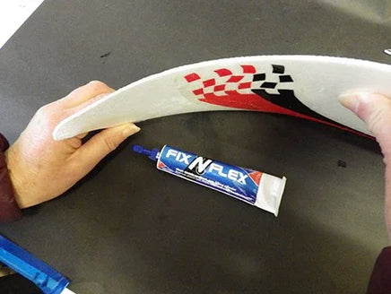 Person holding a curved object with a tube of Fix-N-Lex glue on a dark surface