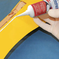 Hand applying white glue to a yellow and blue inflatable boat.
