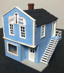 Model of a blue building with 'Craig's Tool Shop' sign on a dark surface.