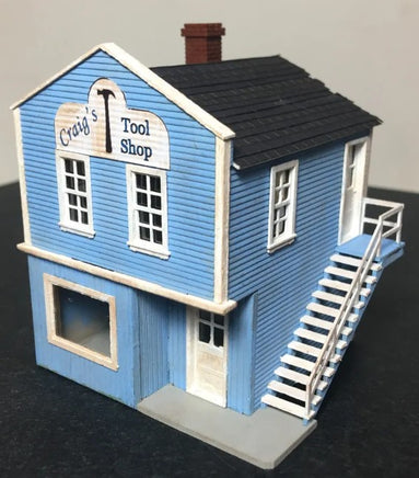 Model of a blue building with 'Craig's Tool Shop' sign on a dark surface.