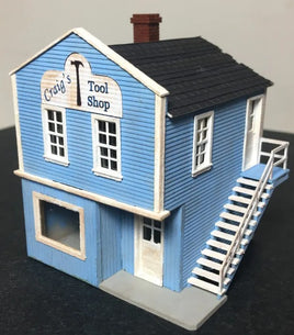 Model of a two-story building with a sign reading 'Craig's Tool Shop' on a dark surface.