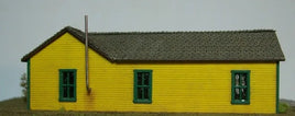 Model of a yellow building with green windows and a gray roof against a plain background