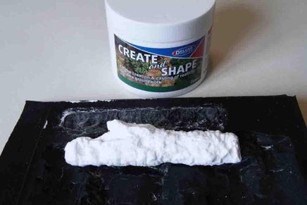 White modeling clay on a black surface with a container labeled 'Create and Shape' in the background.