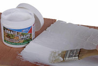 Container of modeling clay, sheets of white paper, and a paintbrush on a wooden surface.