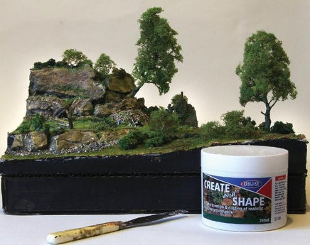 Model landscape with trees and rocks, Faller paint can, and brush on a white background